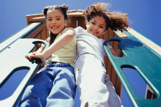 two girls looking down from playground equipment